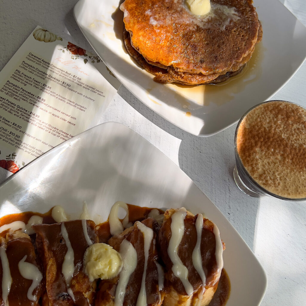 Close-up of a breakfast plate with pancakes topped with butter and syrup, alongside a cinnamon roll with icing and a cup of coffee at The Gilbert House Restaurant.